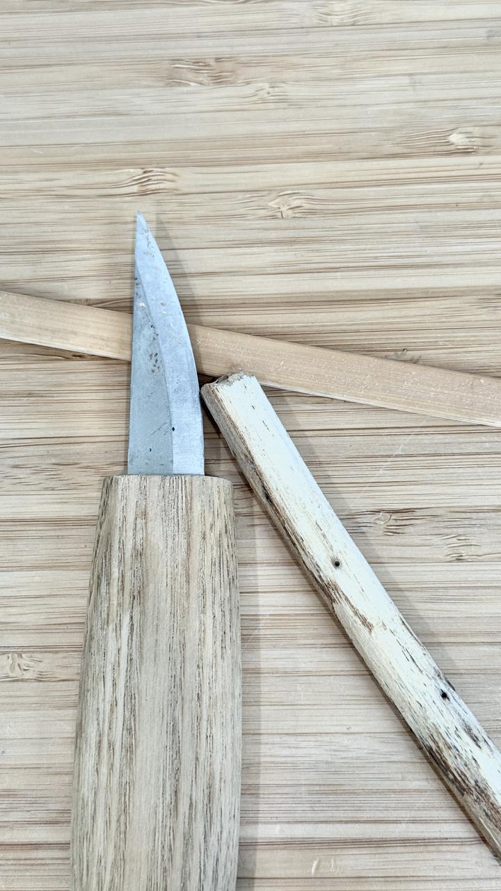 A carving knife beside a half-peeled stick on a bamboo board